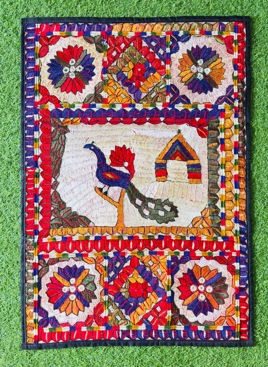 Hand-embroidered Sindhi wall hanging with folk bird and cottage motif — traded through Karvora's UK–Pakistan network